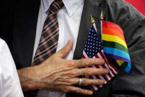 Picture of a Man's Hand Over His Heart, with the U.S. and LGBT Flag In His Shirt Pocket
